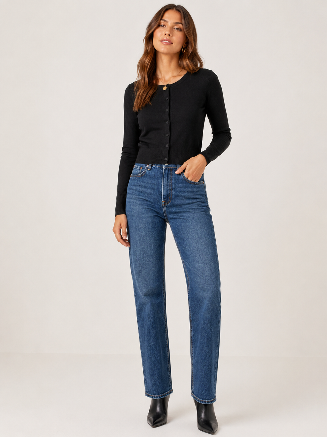A woman modeling a black long-sleeve button-front top and blue straight-leg jeans against a plain light gray studio background.