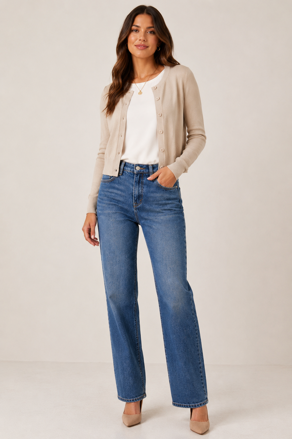 A woman modeling a beige button-up cardigan over a white top and blue high-waisted straight-leg jeans, standing against a plain light beige studio background.