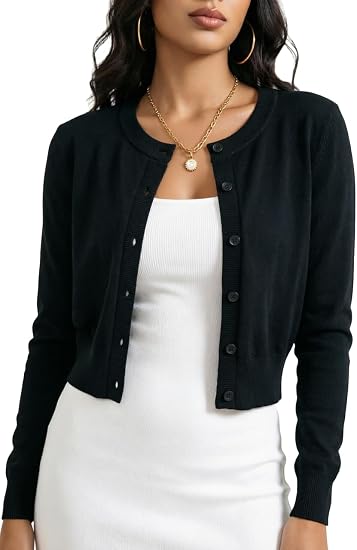 A woman wearing a black cropped button-front cardigan over a white ribbed dress, shown from the shoulders to the hips against a plain white studio background.