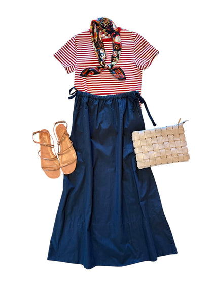 Striped shirt, navy skirt, shoes, and woven bag on a white background