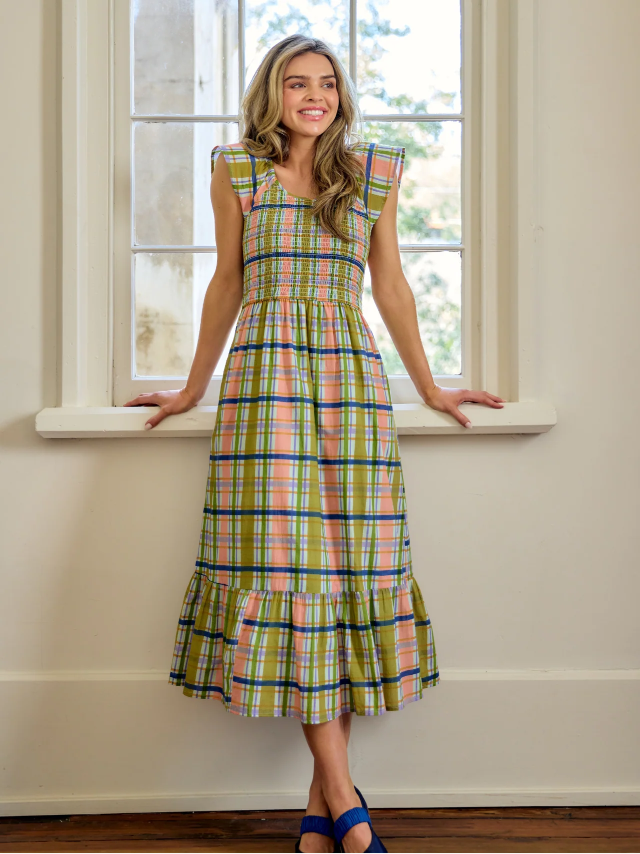 Woman wearing a plaid dress standing by a window