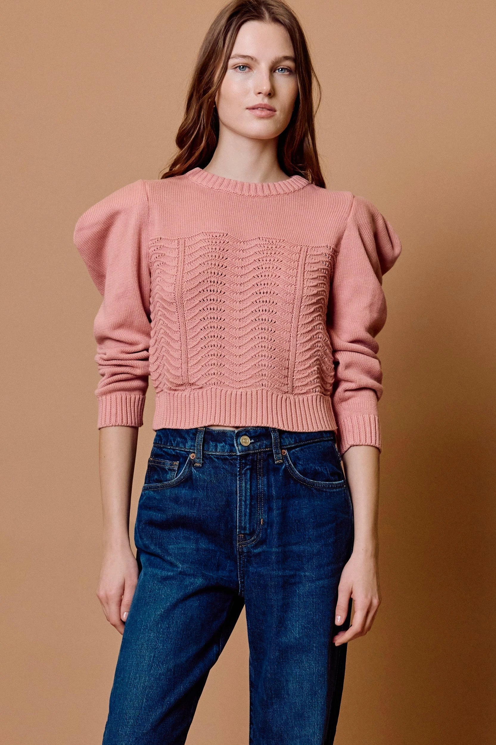 Model wearing cotton blush colored sweater styled with jeans in front of tan backdrop