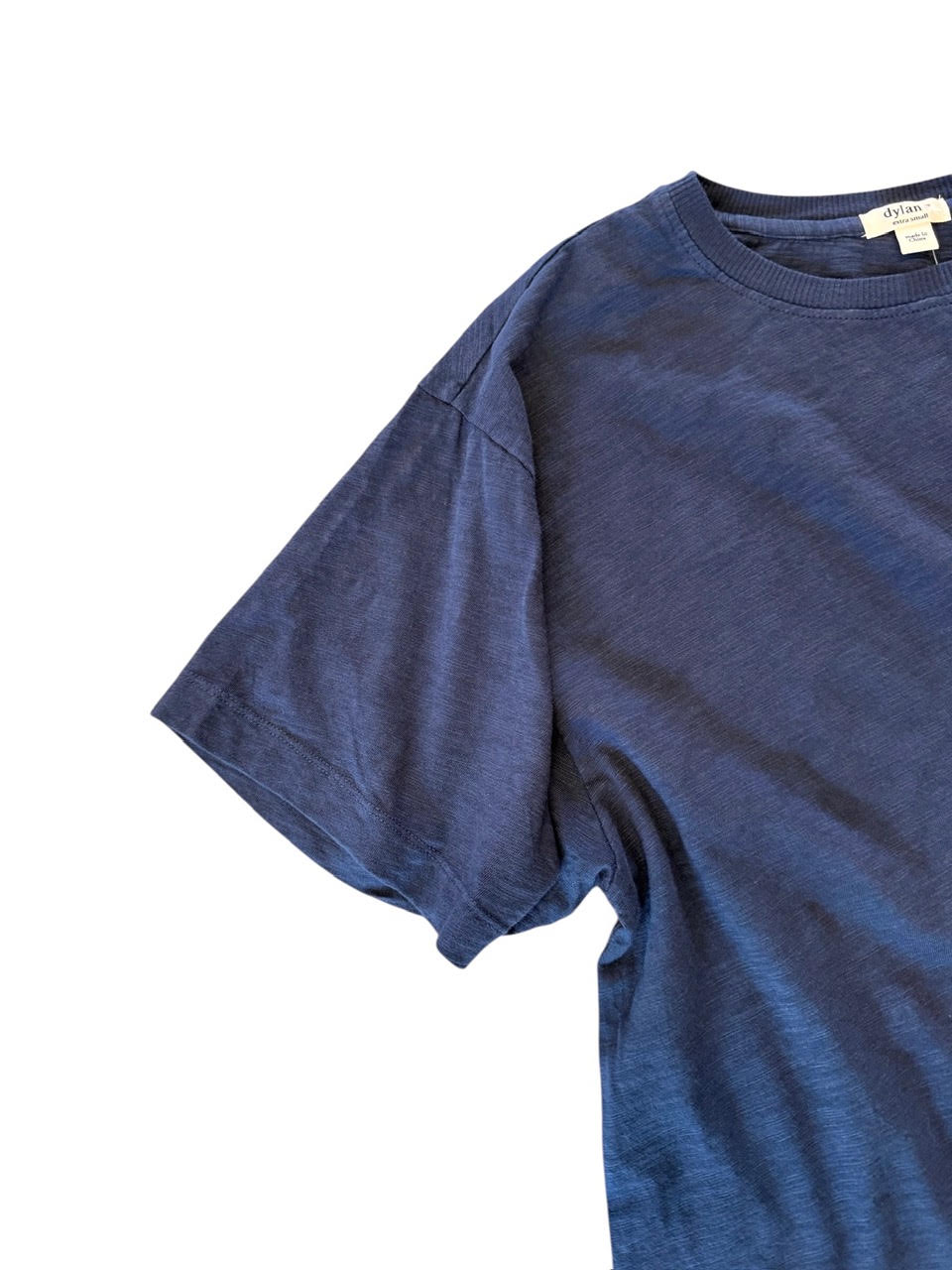 A close-up of a blue short-sleeve crewneck t-shirt laid flat on a white background, showing the fabric texture and a small neck label.