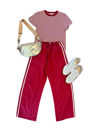 Red and white striped shirt with red pants, silver bag, and white shoes on a wooden floor.